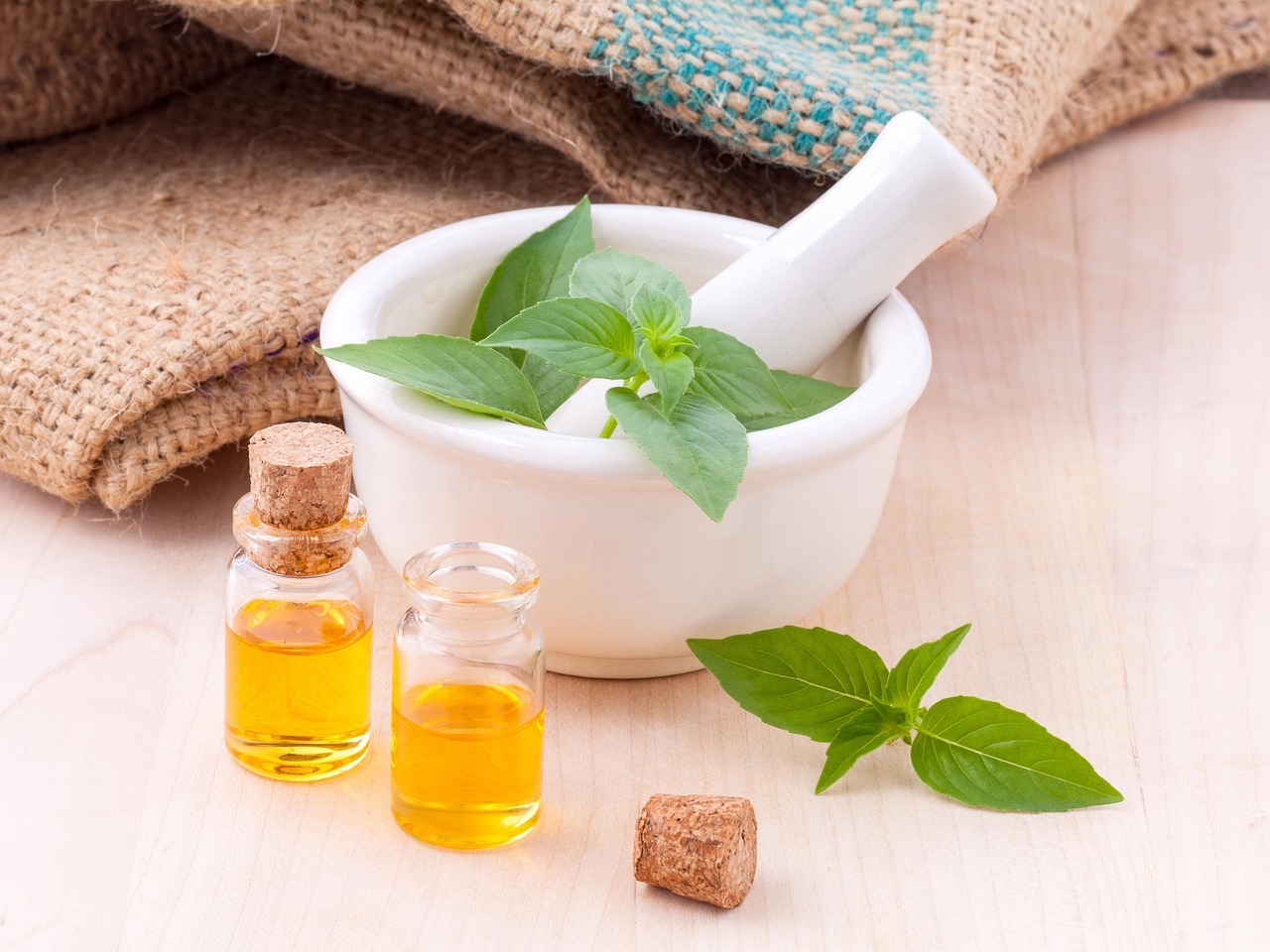 A clean arrangement of a mortar and pestle with mint leaves and small bottles of oil, suggesting wellness or essential oils.