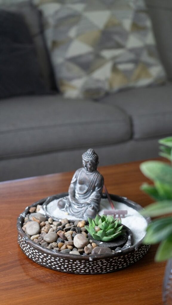 Miniature zen garden with buddha statue on wooden table.
